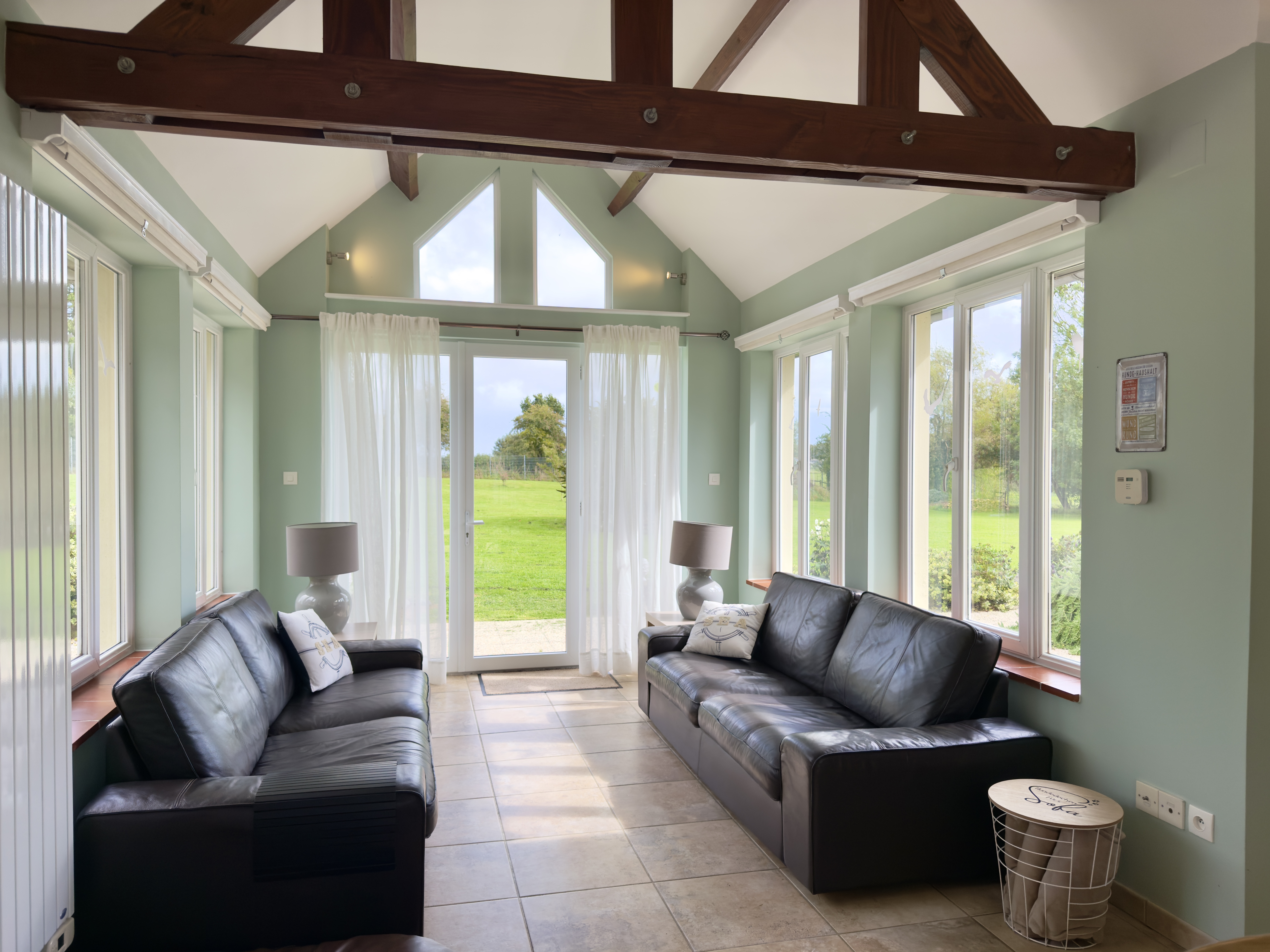 Der Wintergarten von Maison Les Grues mit zwei Ledersofas, Hundedecken, Hundebett. Blick in den großen Garten und das Marschland.